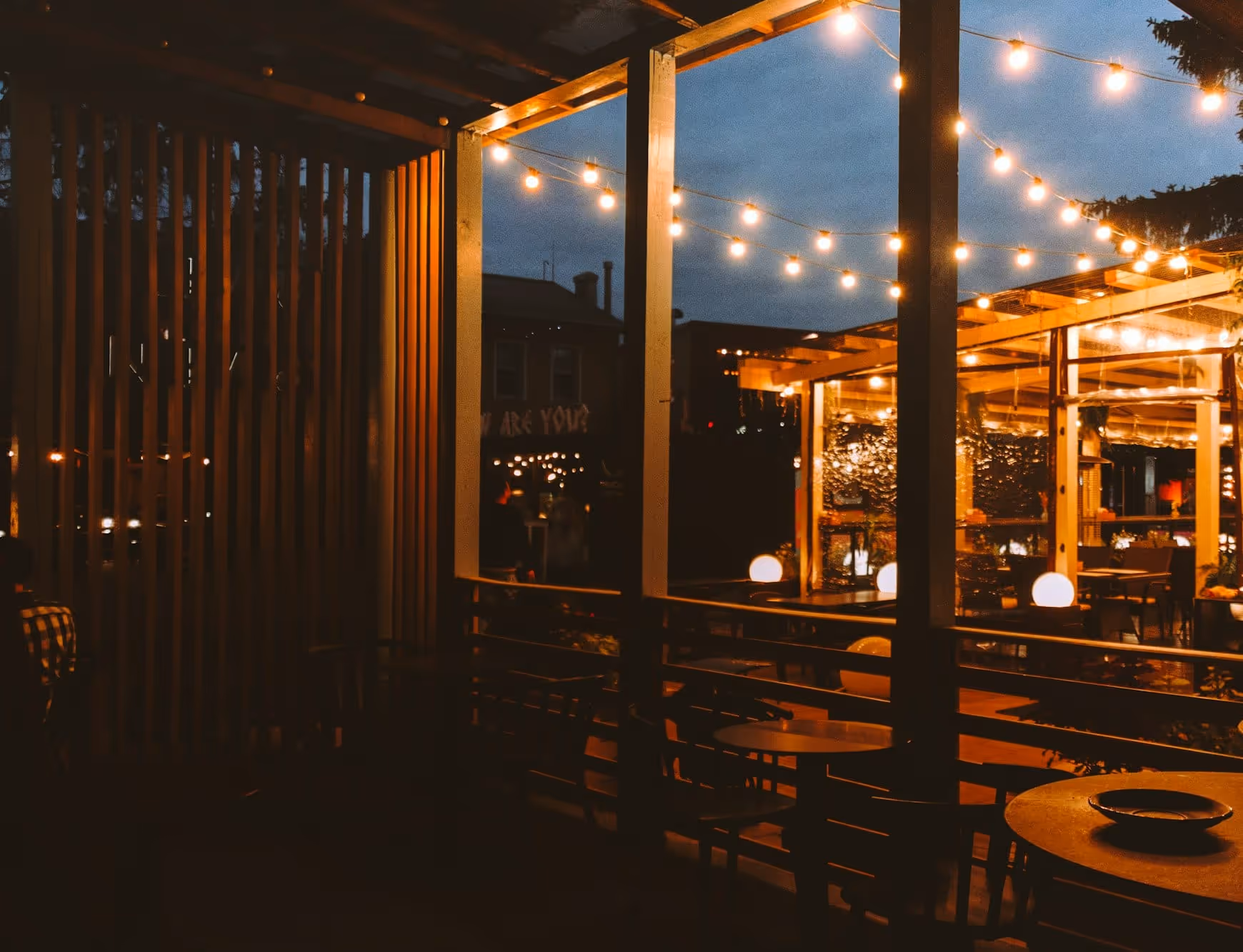 The Cortland Street patio at dusk, strung with bulb lights over wooden tables under the pergola
