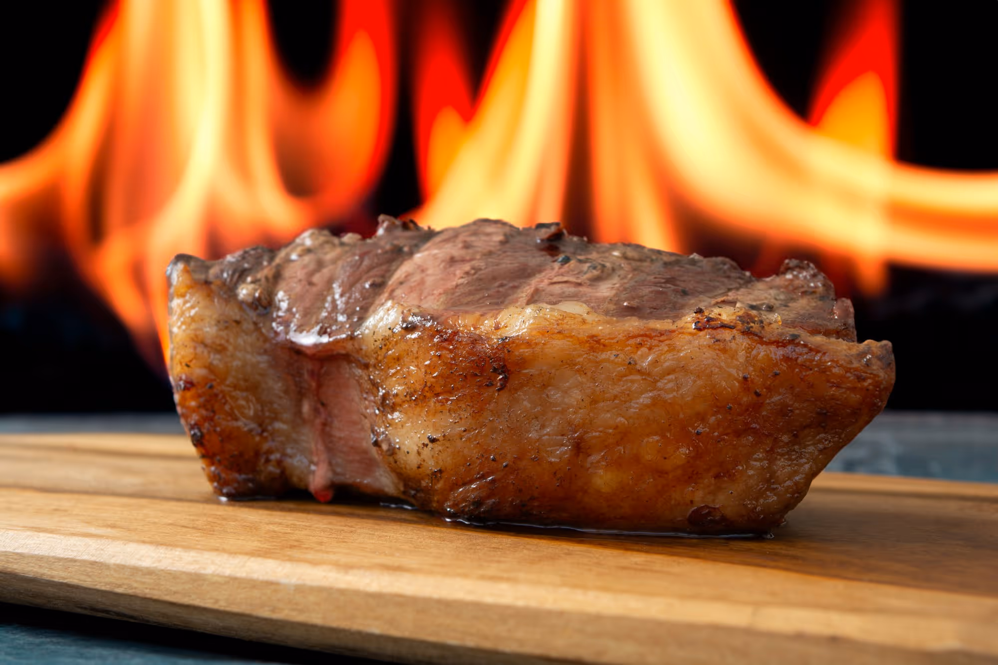 A rested ribeye on a wooden board in front of the open flame of the oven