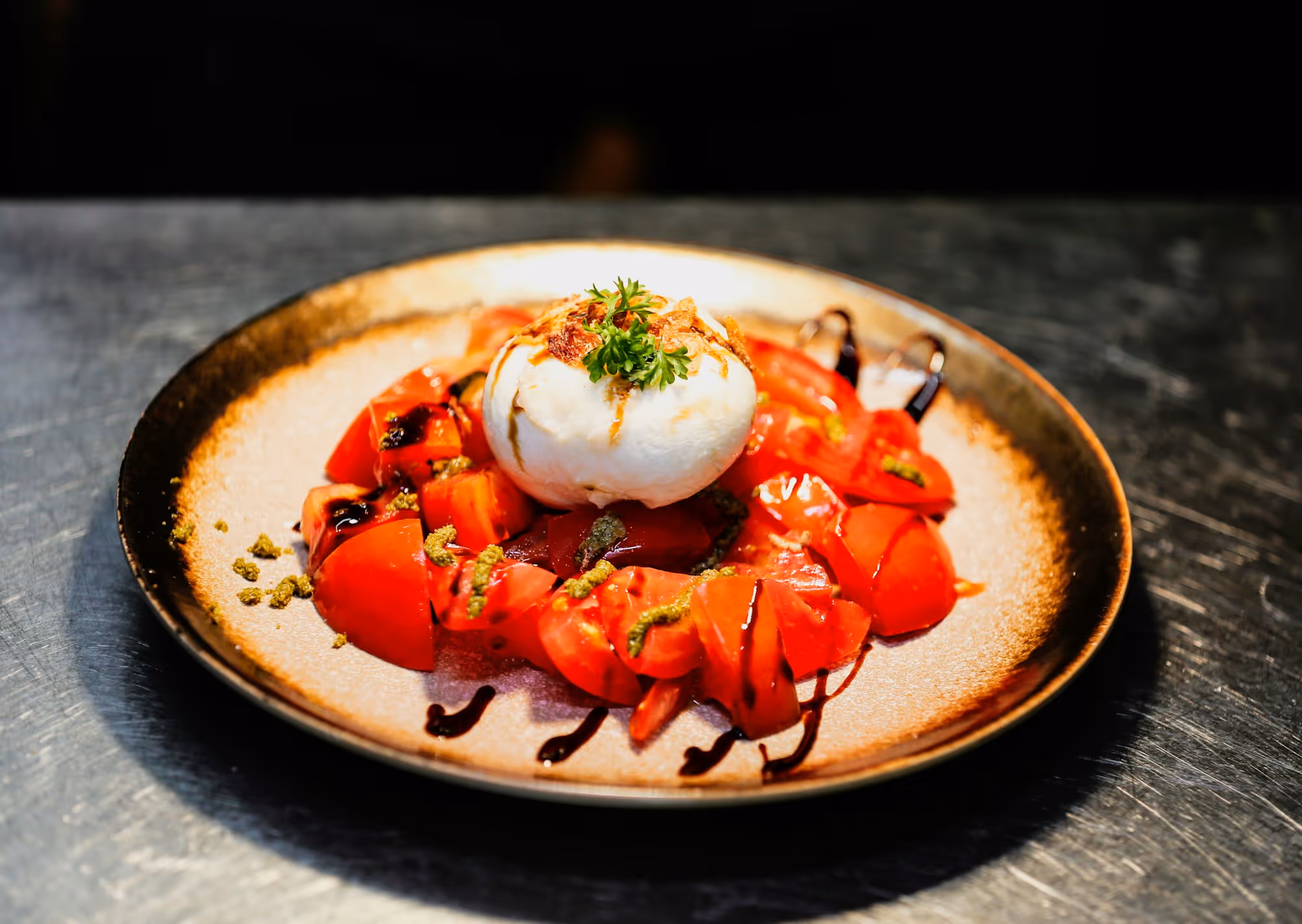 Burrata di Andria on a terracotta-rimmed plate, ringed with charred tomatoes and aged balsamic