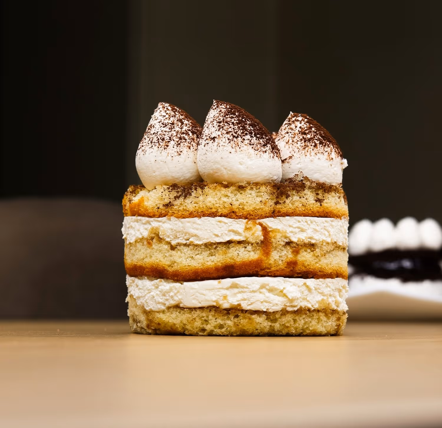 A slab of house tiramisu cut to show three layers of savoiardi and mascarpone under cocoa