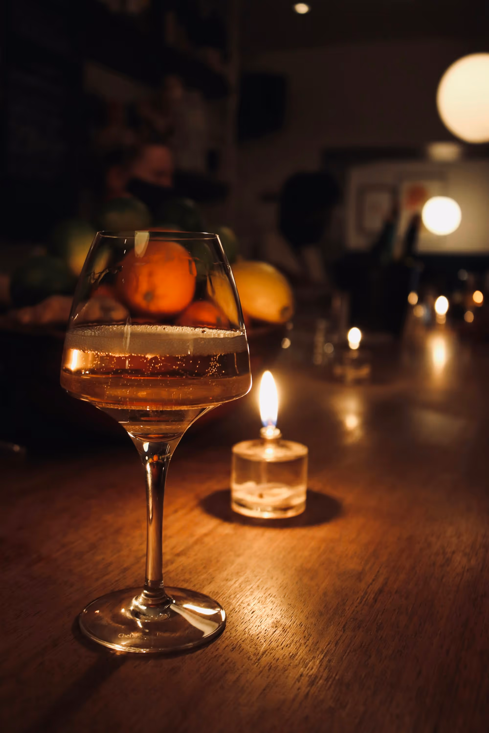 A glass of rosato beside a lit candle on the bar top at the end of service