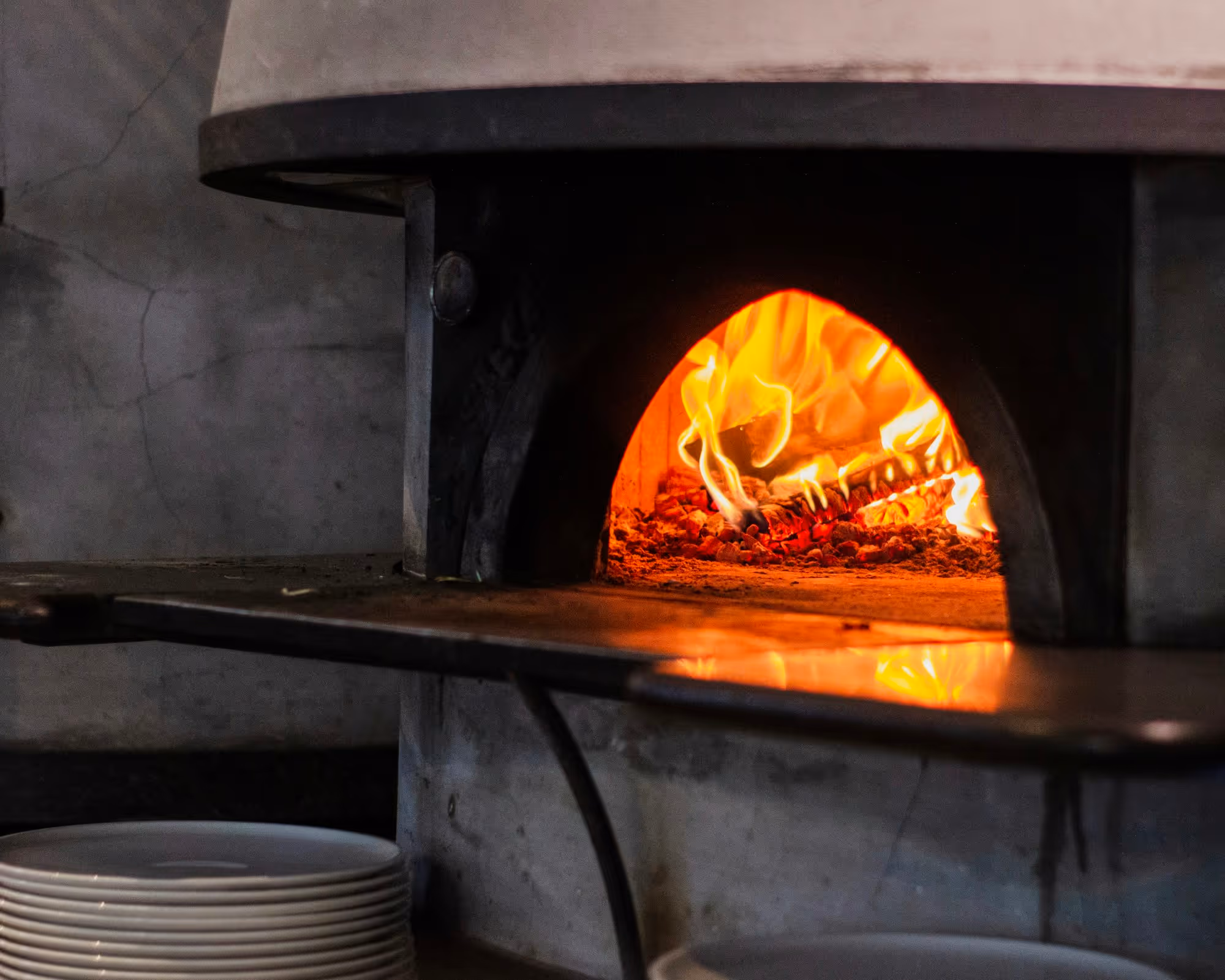 Oak burning at the back of the wood oven with the peel resting across the mouth and plates stacked below